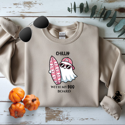 Beige sweatshirt with a ghost holding a Boo Board graphic and text on a wooden surface with pumpkins and leaves.