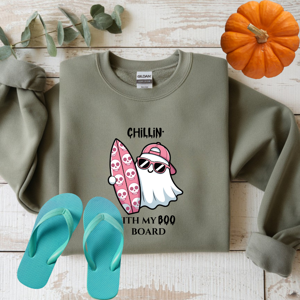 Green sweatshirt with ghost and surfboard graphic, teal flip-flops, and small pumpkin on wooden surface