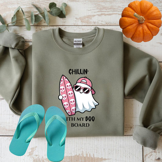 Green sweatshirt with ghost and surfboard graphic, teal flip-flops, and small pumpkin on wooden surface