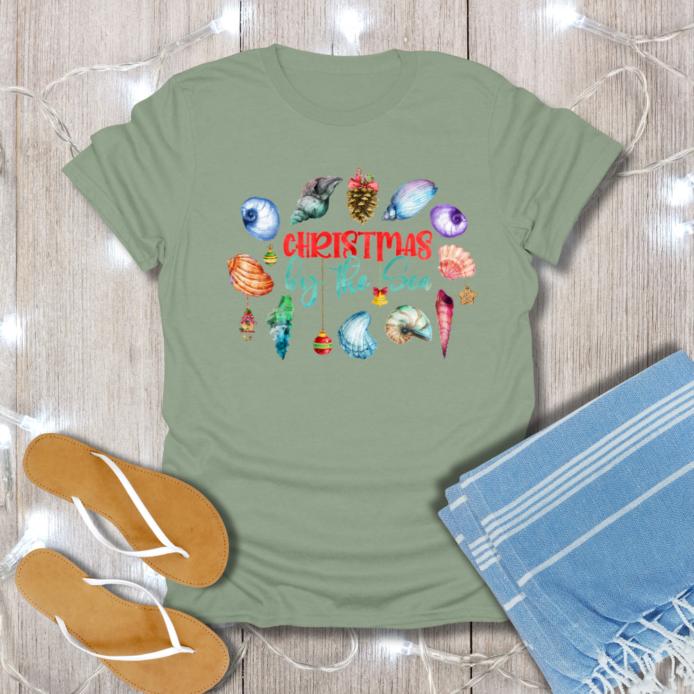 Green t-shirt with Christmas-themed design on a wooden surface with flip-flops and a towel.