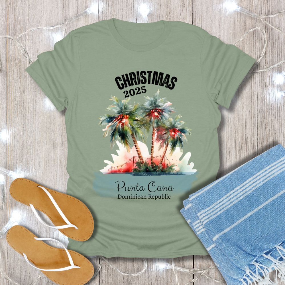 Green t-shirt with Christmas 2025 Punta Cana Dominican Republic design on a wooden surface with flip-flops and a towel.