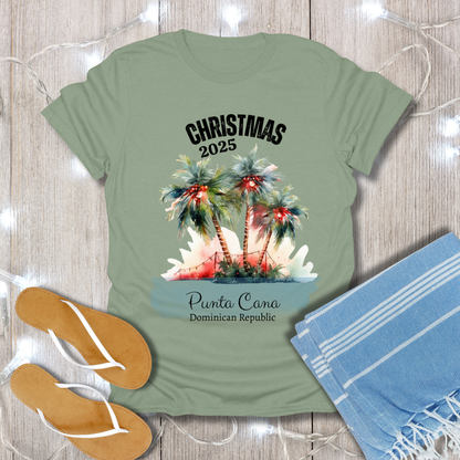 Green t-shirt with Christmas 2025 Punta Cana Dominican Republic design on a wooden surface with flip-flops and a towel.