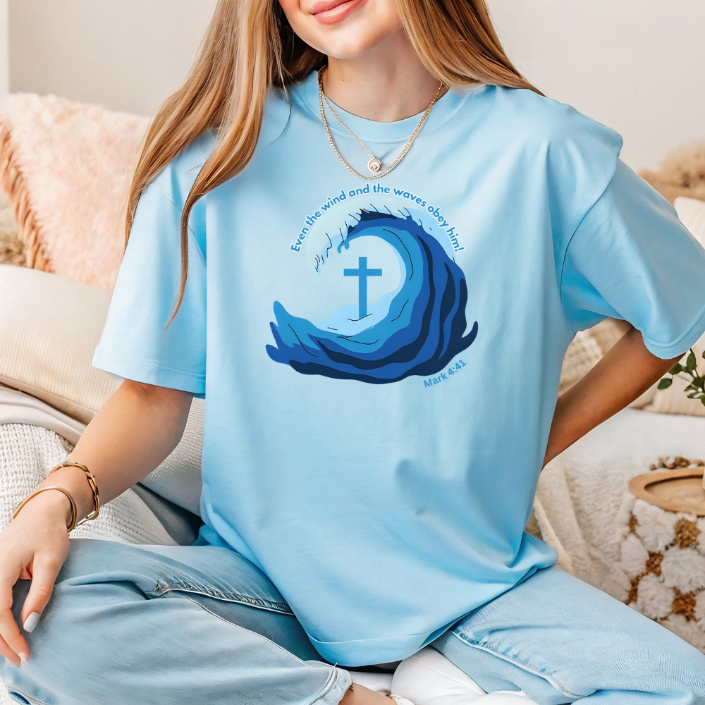 Person wearing a light blue t-shirt with a wave and cross design, sitting on a couch.