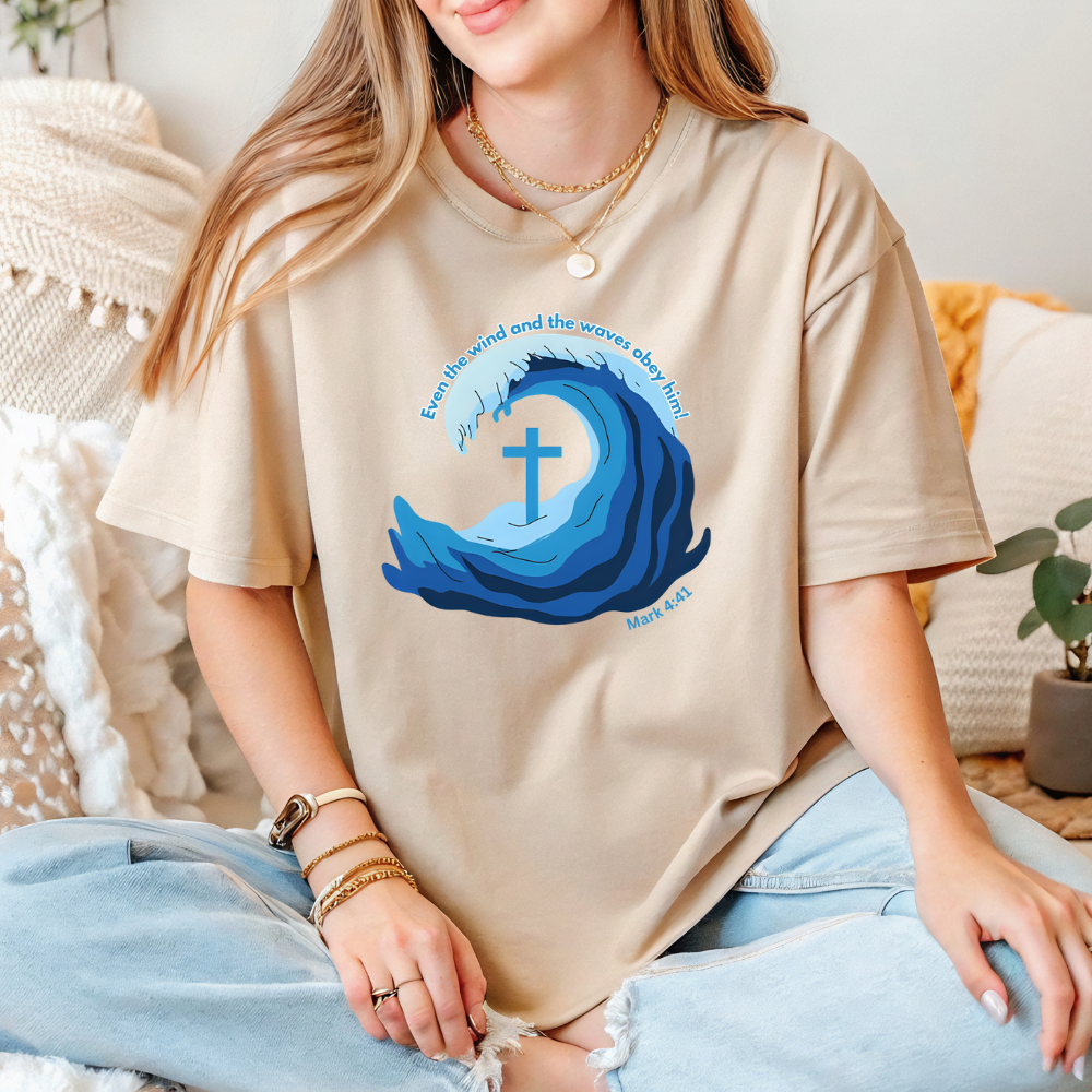 Person wearing a beige t-shirt with a blue wave design and cross, sitting on a couch.