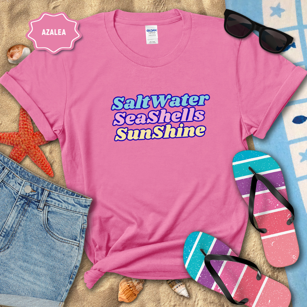 Pink t-shirt with 'Salt Water Sea Shells Sunshine' text, sunglasses, flip-flops, and beach items on sand.