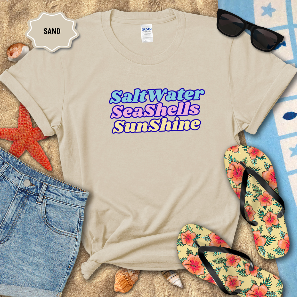 Beige t-shirt with 'Salt Water Seashells Sunshine' text, sunglasses, flip-flops, and beach items on sand.