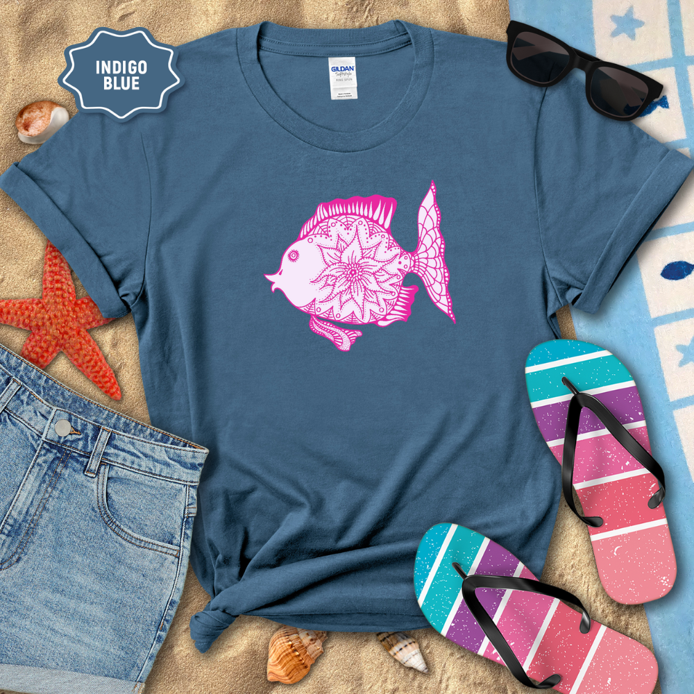 Indigo blue t-shirt with pink fish design on a beach setting with sunglasses, flip-flops, and denim shorts.