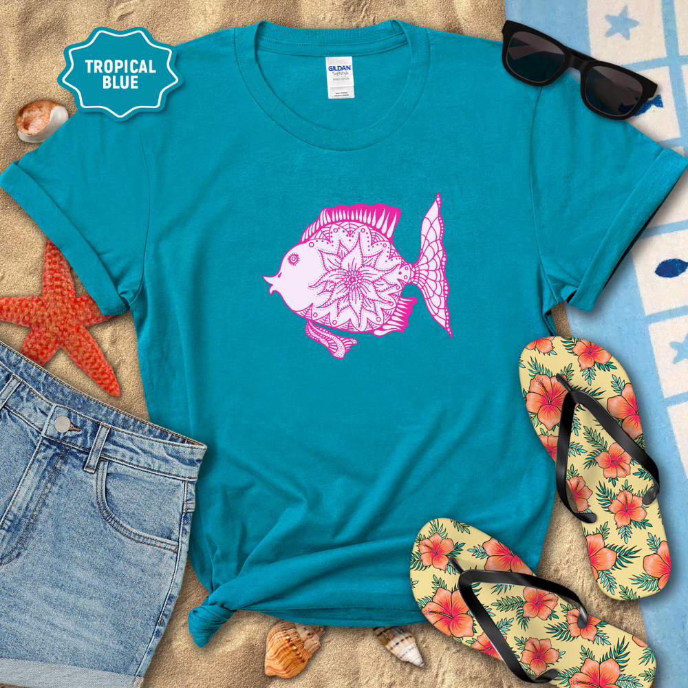 Blue t-shirt with pink fish design on a sandy background with flip-flops and sunglasses.