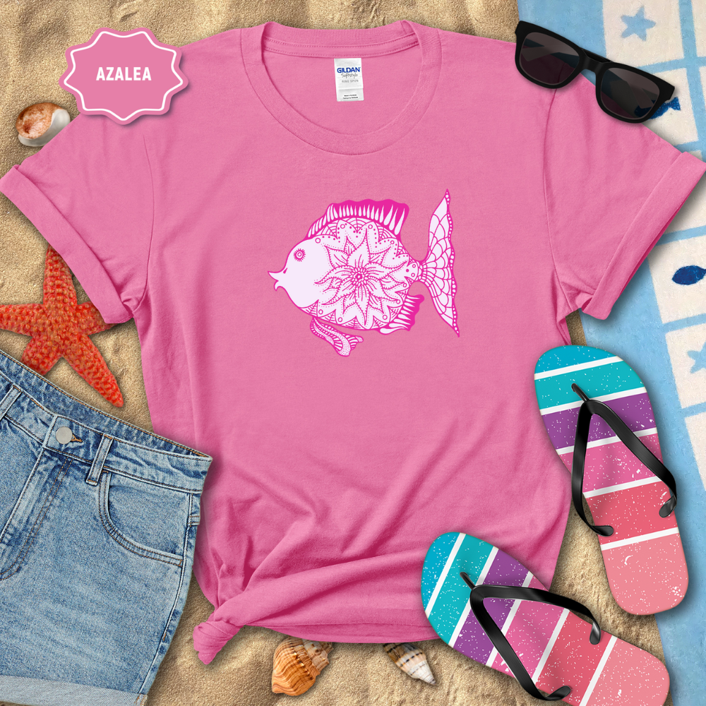 Pink t-shirt with a fish design on a beach setting with sunglasses, flip-flops, and denim shorts.