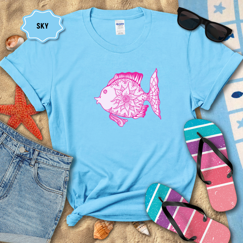 Blue t-shirt with pink fish design on a sandy background with beach accessories.