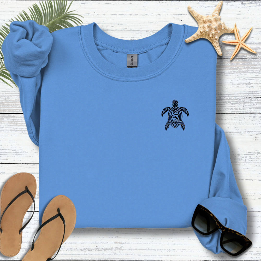 Blue sweatshirt with a turtle design on a wooden surface with flip-flops and sunglasses.