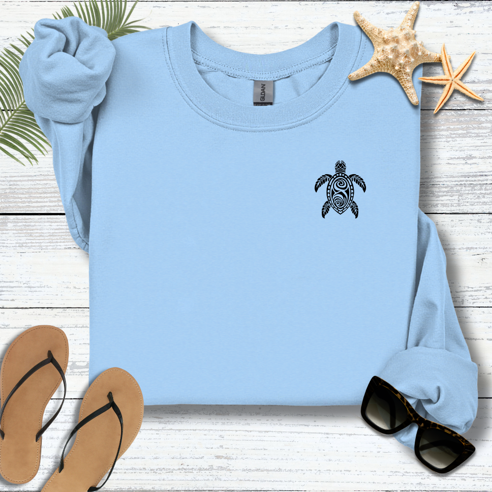 Light blue sweatshirt with a turtle design on a wooden surface with flip-flops and sunglasses.