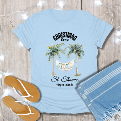 Light blue t-shirt with palm tree and hammock design, placed on a wooden surface with flip-flops and a towel.
