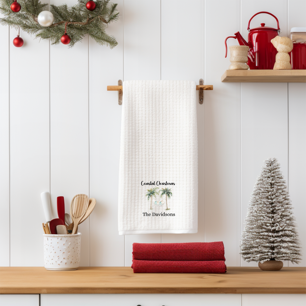 Kitchen setting with a towel rack featuring a personalized towel, red towels, and Christmas decorations.