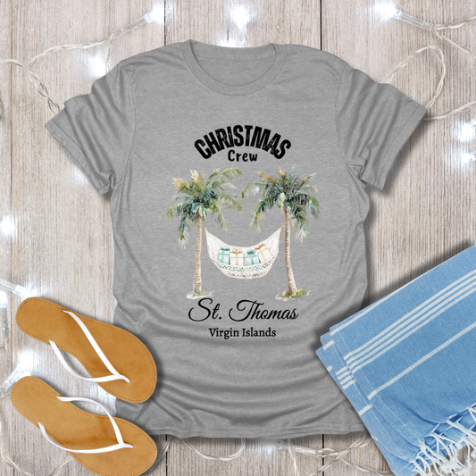 Gray t-shirt with tropical design and text on a wooden surface with flip-flops and a towel.