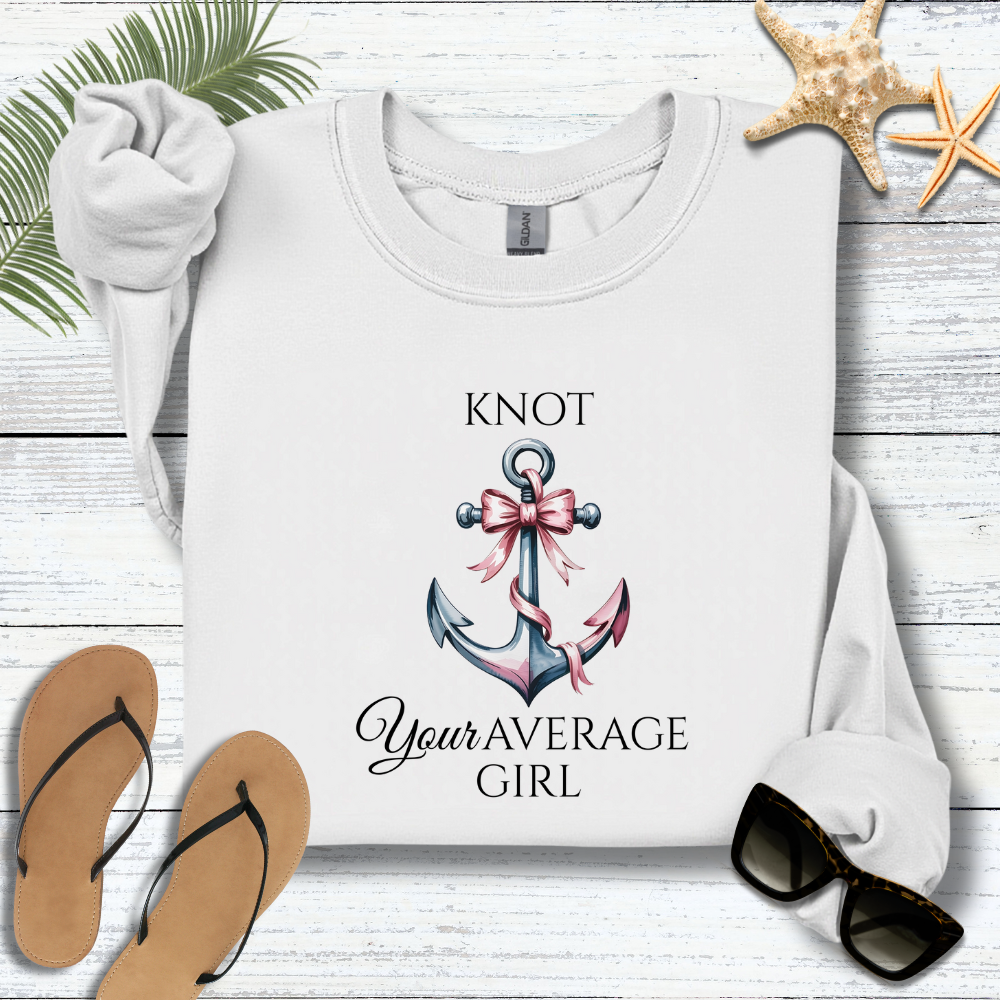 White sweatshirt with anchor design and text on a wooden surface with flip-flops and sunglasses.