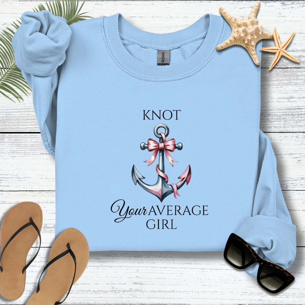 Light blue sweatshirt with anchor and bow design on a wooden surface with flip-flops and sunglasses.