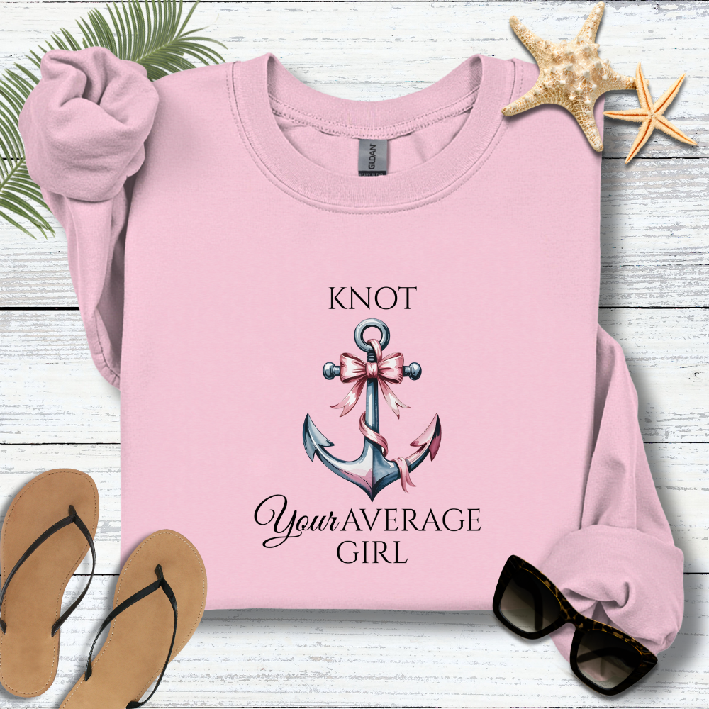 Pink sweatshirt with anchor design and text on a wooden surface with accessories.