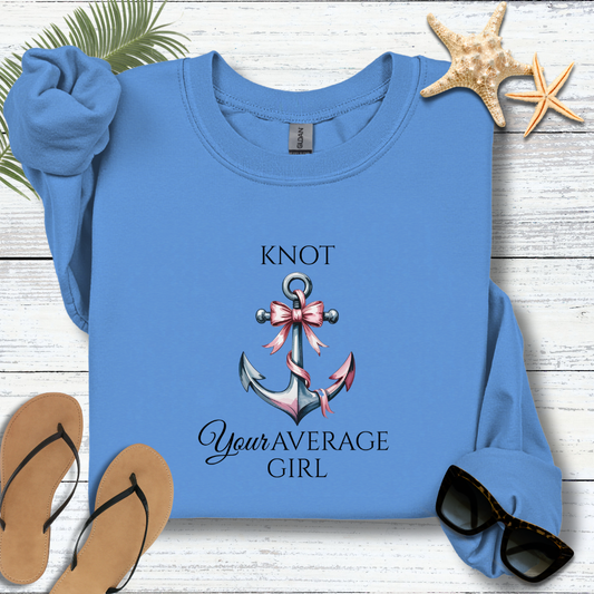 Blue sweatshirt with anchor and bow design on a wooden surface with flip-flops and sunglasses.