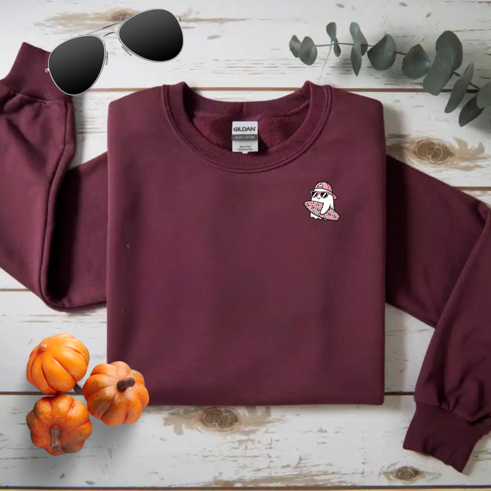 Maroon sweatshirt with a small logo on a wooden surface with pumpkins and sunglasses.