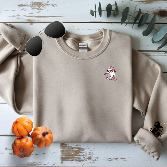 Beige sweatshirt with a small graphic on a wooden surface with pumpkins and leaves.
