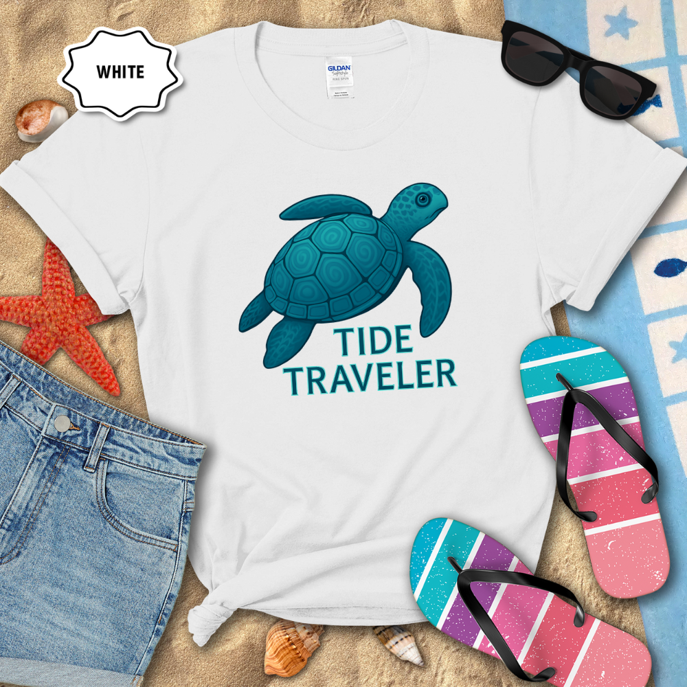 White t-shirt with blue turtle graphic and 'Tide Traveler' text on a sandy background with beach accessories.