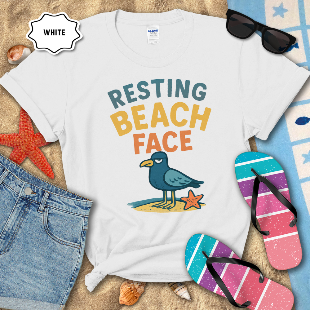 White t-shirt with 'Resting Beach Face' design on sand with beach accessories.