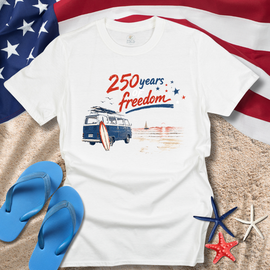 White t-shirt with '250 years freedom' design on a beach setting with American flag, flip-flops, and starfish.