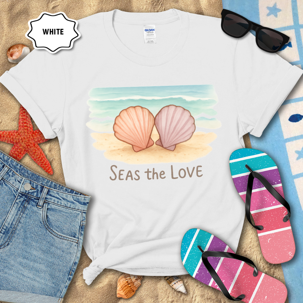 White t-shirt with shell design and 'Seas the Love' text on a beach-themed background with sunglasses, flip-flops, and denim shorts.