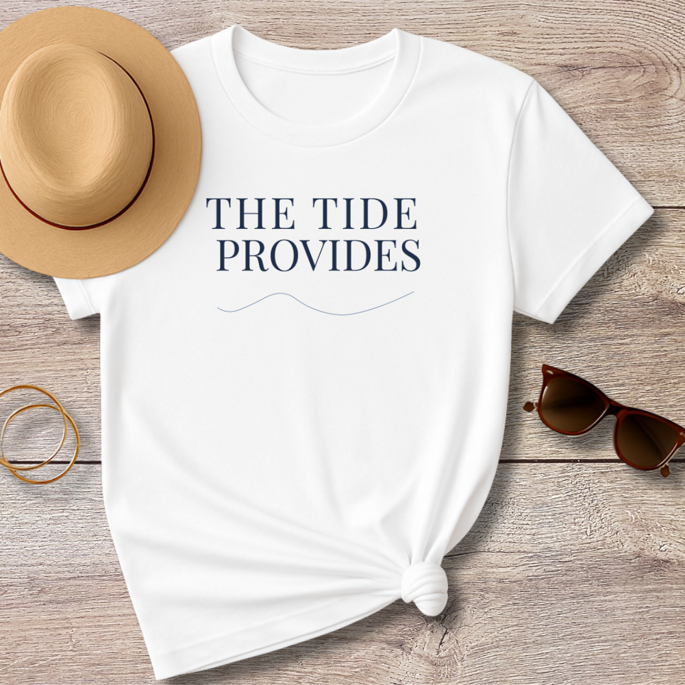 White t-shirt with 'THE TIDE PROVIDES' text, sun hat, sunglasses, and bracelet on a wooden surface