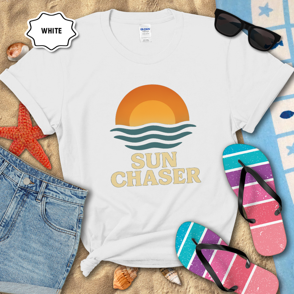 White t-shirt with 'Sun Chaser' design on a sandy background with sunglasses, flip-flops, and denim shorts.