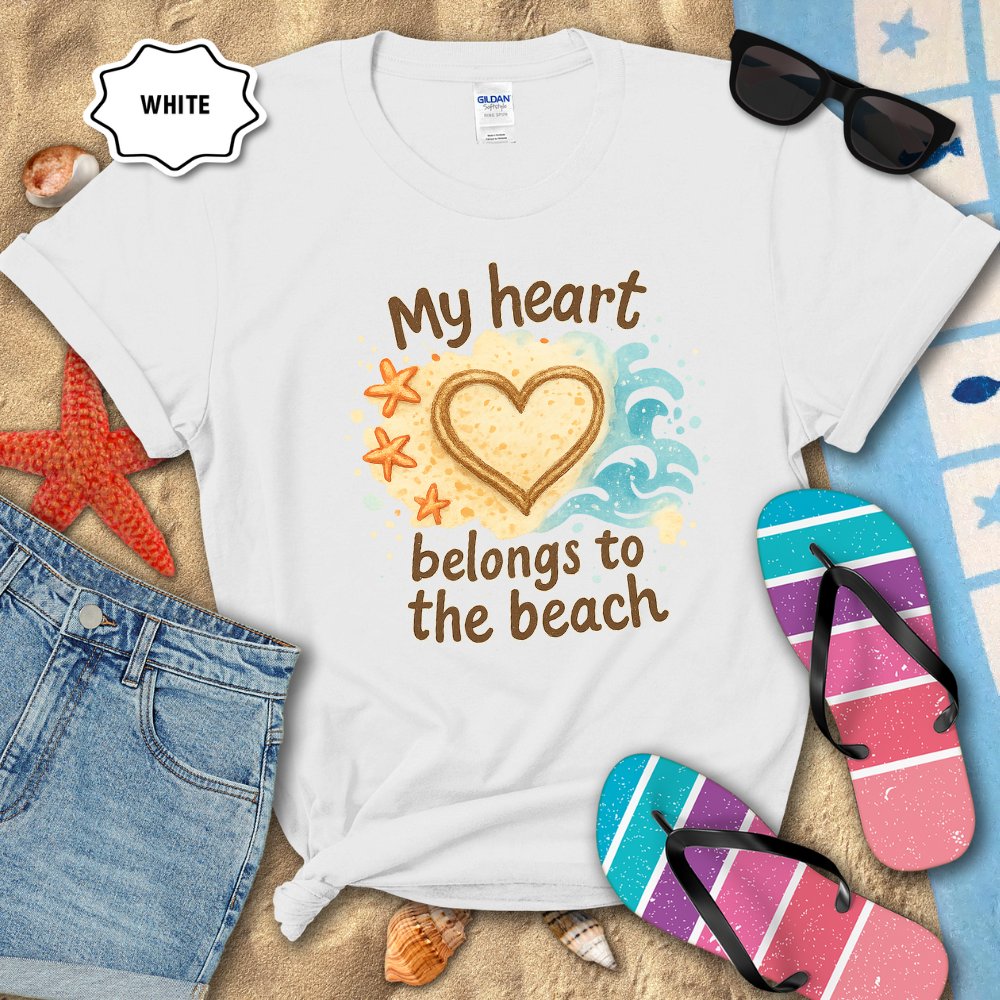 White t-shirt with 'My heart belongs to the beach' design on sand with sunglasses, flip-flops, and denim shorts.