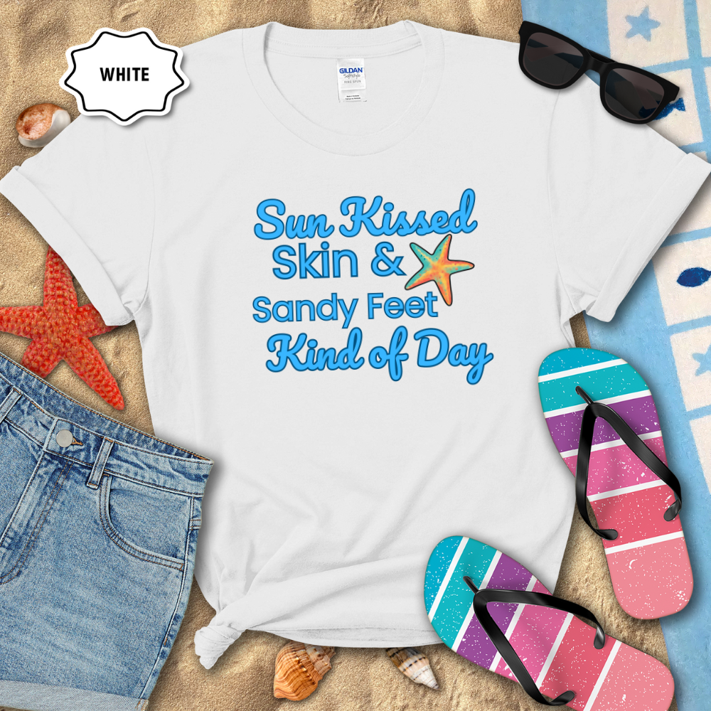 White t-shirt with beach-themed text on a sandy background with flip-flops and sunglasses.