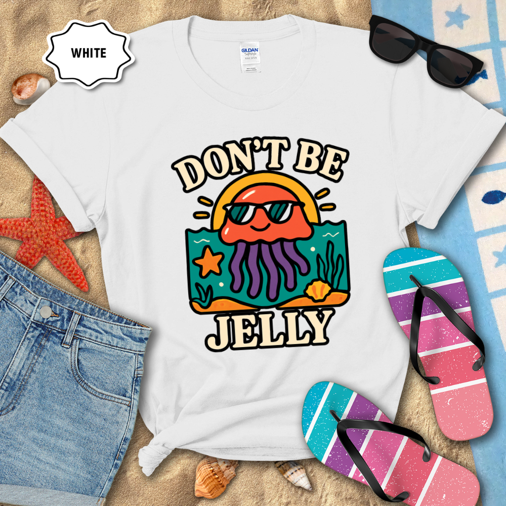 White t-shirt with 'Don't Be Jelly' design on a beach-themed background with sunglasses, flip-flops, and denim shorts.