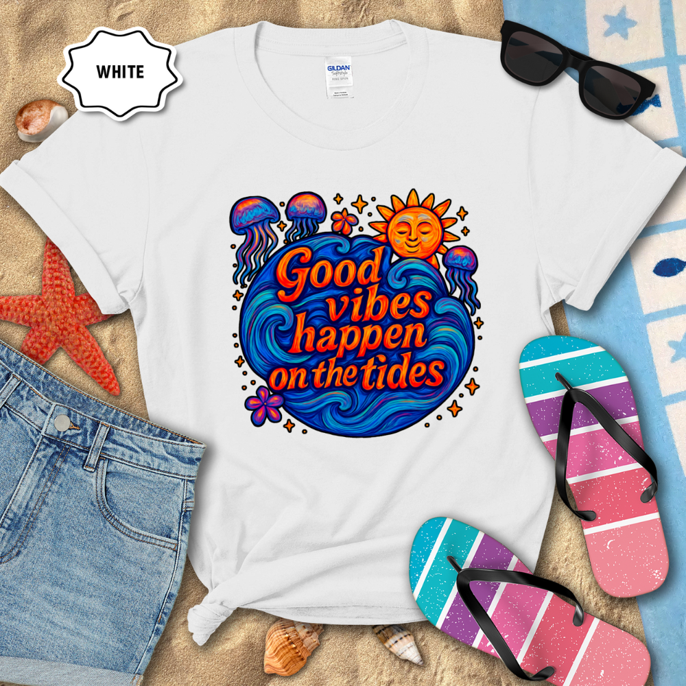 White t-shirt with 'Good vibes happen on the tides' design, sunglasses, flip-flops, and beach accessories on sand.