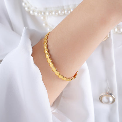 Gold bracelet on a wrist with a pearl necklace in the background
