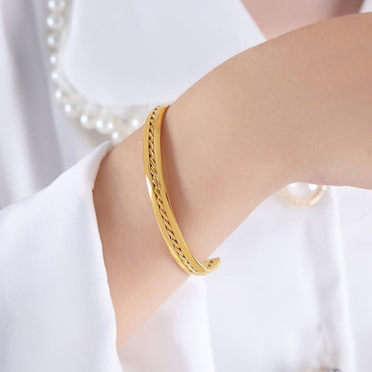 Gold bracelet on a person's wrist with a blurred pearl necklace in the background