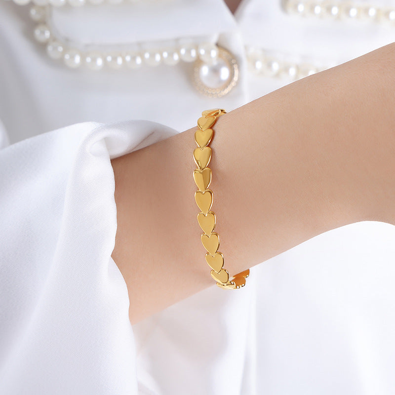 Gold bracelet with heart-shaped links on a wrist against a white background