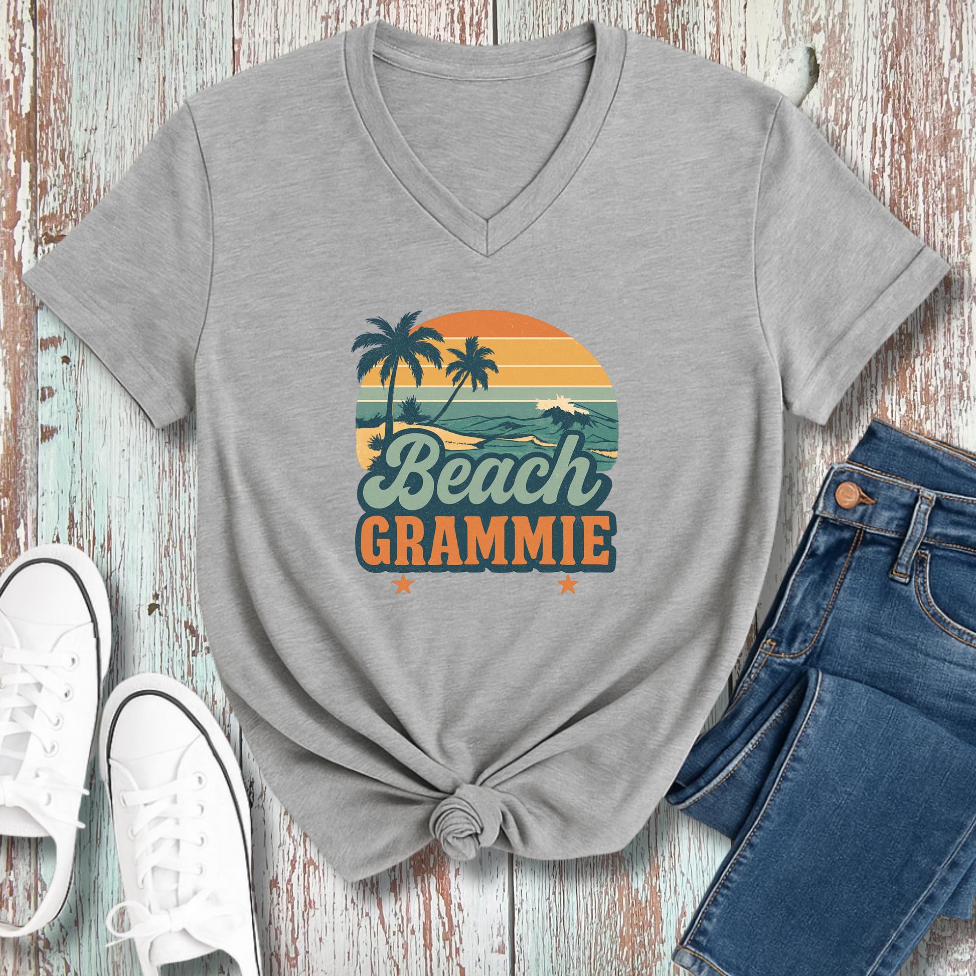 Gray t-shirt with 'Beach Grammie' design on a wooden surface with jeans and sneakers.