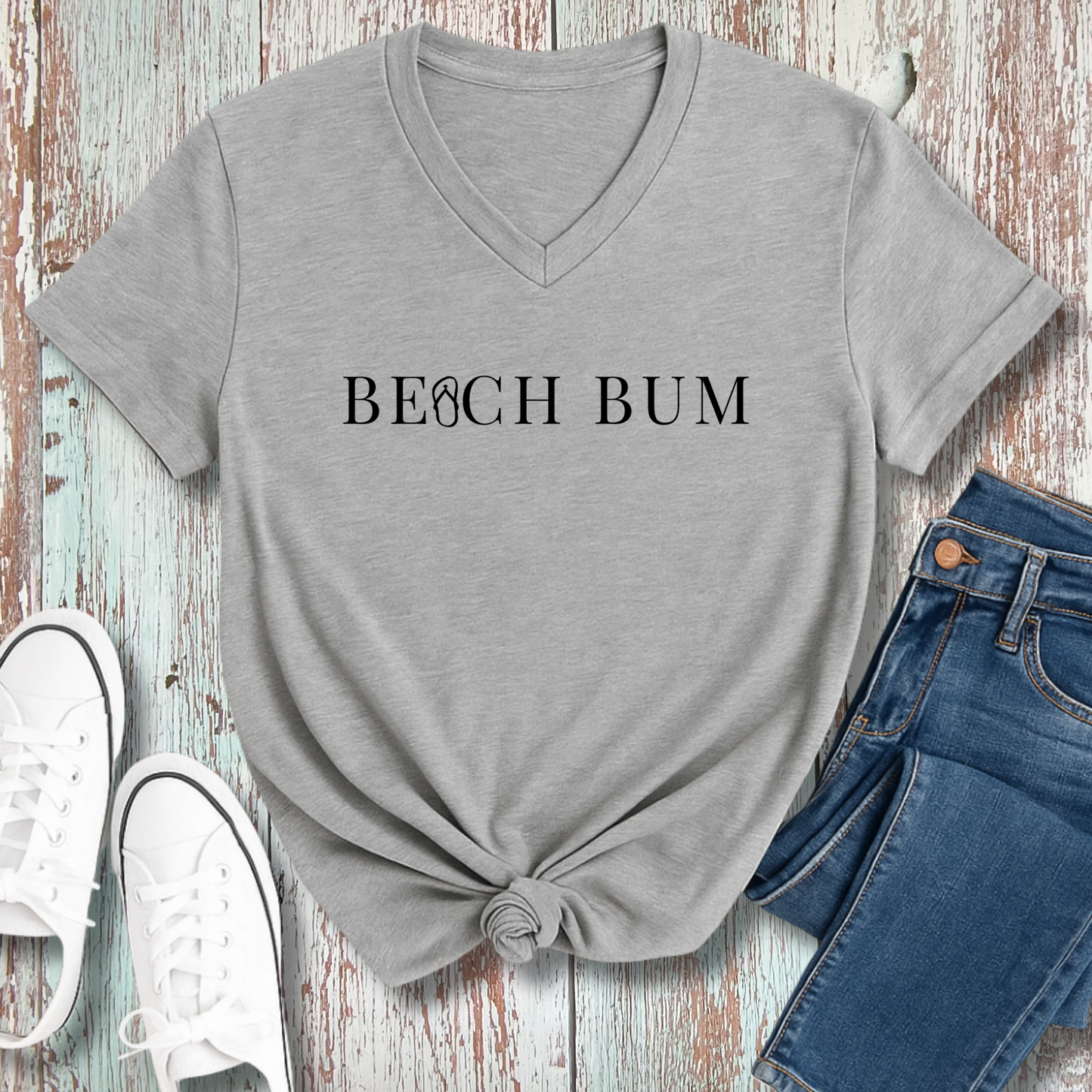 Gray t-shirt with 'BEACH BUM' text, paired with jeans and white sneakers on a wooden surface.