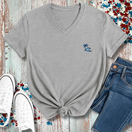 Gray t-shirt with a palm tree and wave design, paired with blue jeans and white sneakers on a wooden surface.