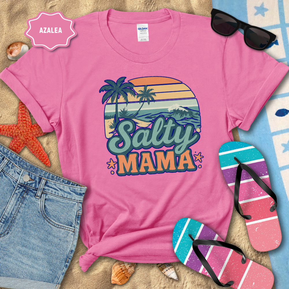 Pink t-shirt with 'Salty Mama' design on a beach-themed background with sunglasses, flip-flops, and denim shorts.