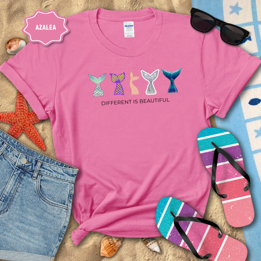 Pink t-shirt with mermaid tail designs and 'Different is Beautiful' text, surrounded by beach items.