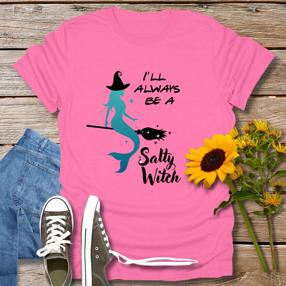 Pink t-shirt with mermaid graphic and text on a wooden surface with jeans and sunflowers.