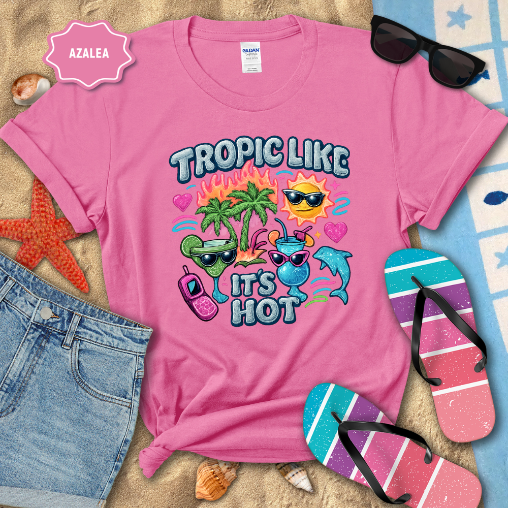 Pink t-shirt with tropical-themed design on a beach setting with sunglasses, flip-flops, and denim shorts.