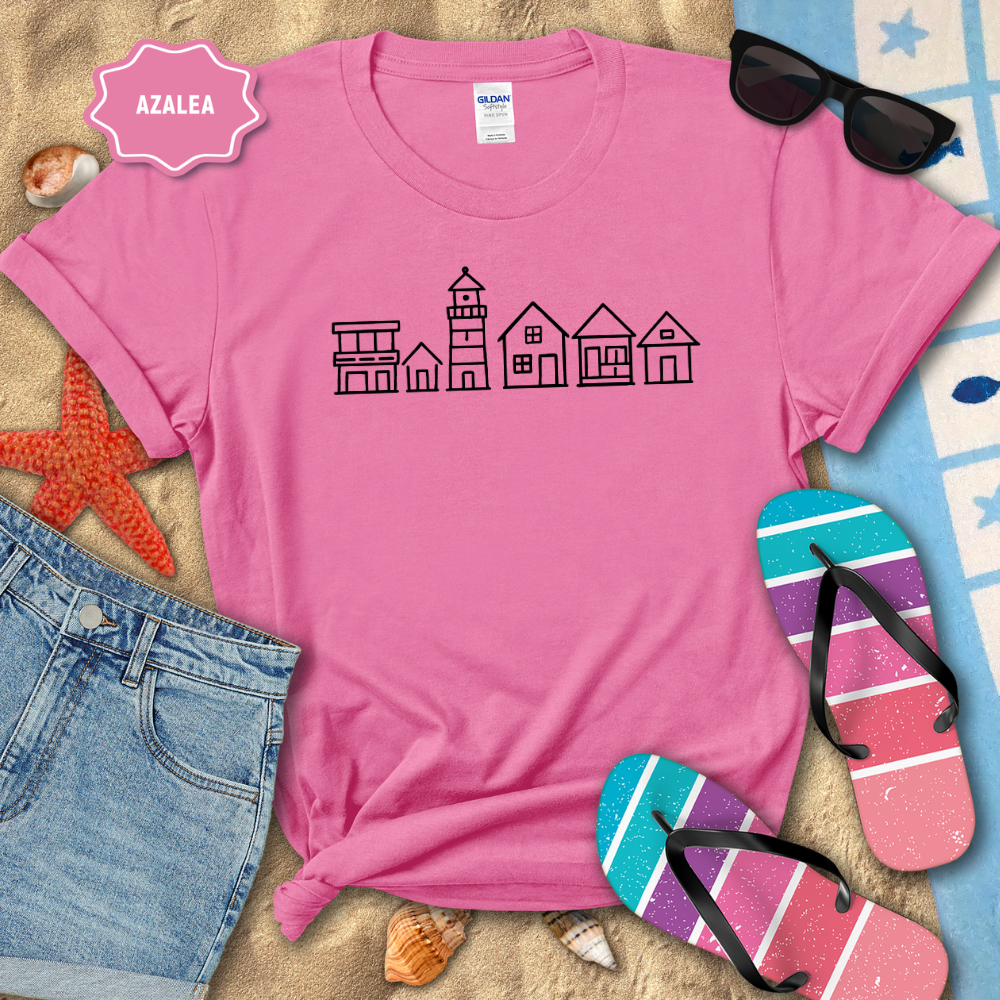 Pink t-shirt with a lighthouse design on a beach setting with sunglasses, flip-flops, and denim shorts.