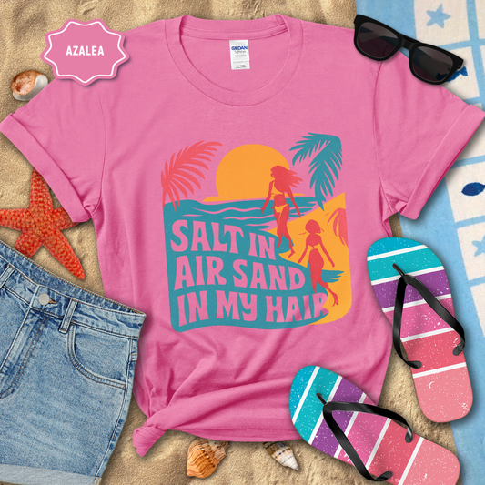 Pink t-shirt with beach-themed design and accessories on sand