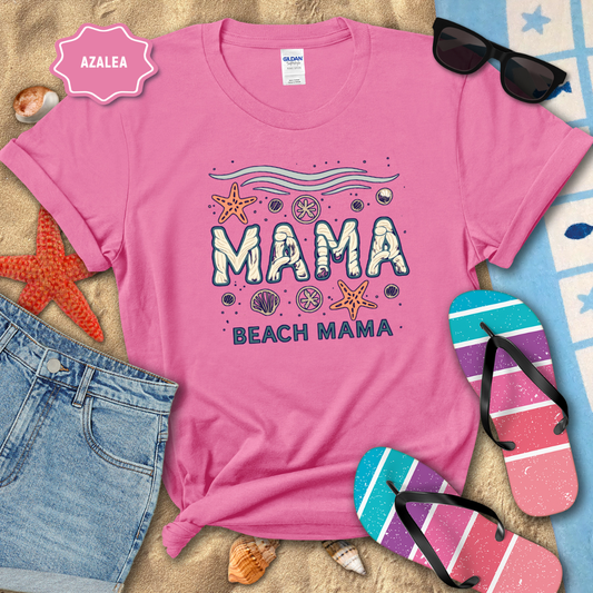 Pink t-shirt with 'Mama Beach Mama' design on a sandy background with beach accessories.
