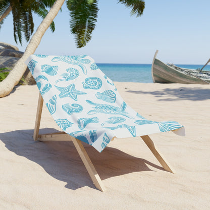 Starfish and turtle print towel draped over a wooden beach chair in the sand