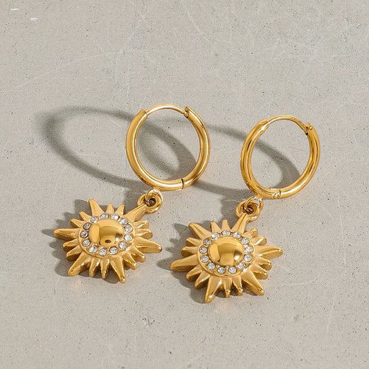 Gold hoop earrings with sunflower-shaped charms on a gray background
